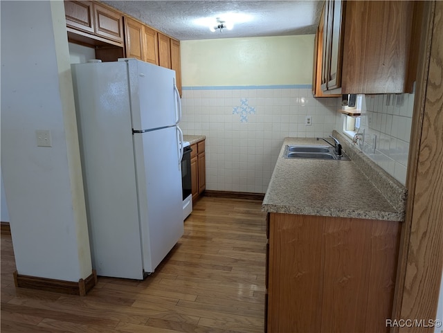 kitchen with a textured ceiling, white appliances, sink, tile walls, and light hardwood / wood-style floors