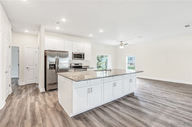 kitchen with light stone countertops, stainless steel appliances, a kitchen island with sink, white cabinets, and light hardwood / wood-style floors