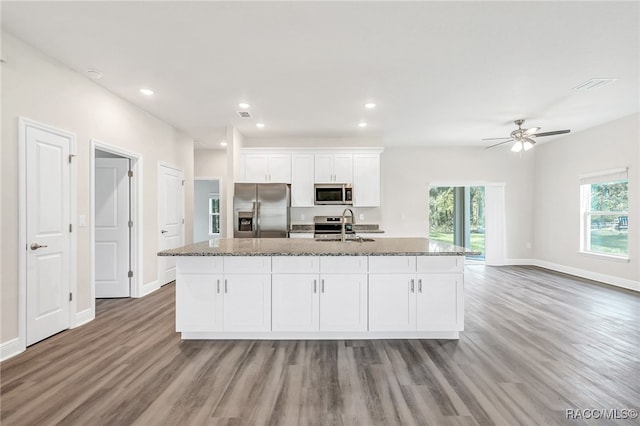 kitchen featuring a kitchen island with sink, dark stone counters, hardwood / wood-style flooring, white cabinetry, and stainless steel appliances