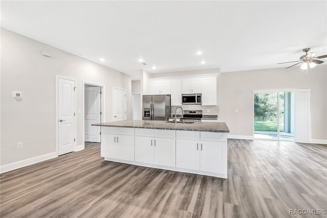 kitchen featuring dark stone counters, stainless steel appliances, white cabinets, light hardwood / wood-style floors, and an island with sink