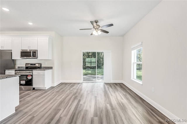 kitchen featuring white cabinetry, ceiling fan, stainless steel appliances, dark stone countertops, and light wood-type flooring