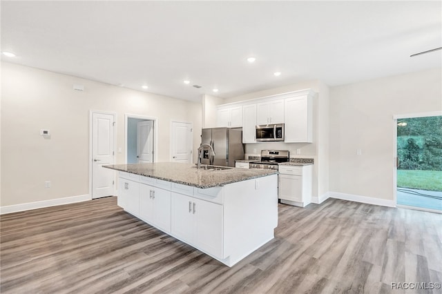 kitchen with appliances with stainless steel finishes, light wood-type flooring, white cabinetry, and an island with sink