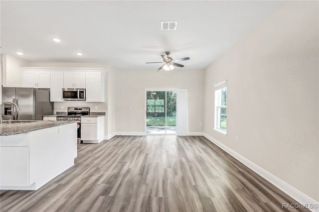 kitchen with light stone countertops, white cabinetry, light wood-type flooring, and appliances with stainless steel finishes