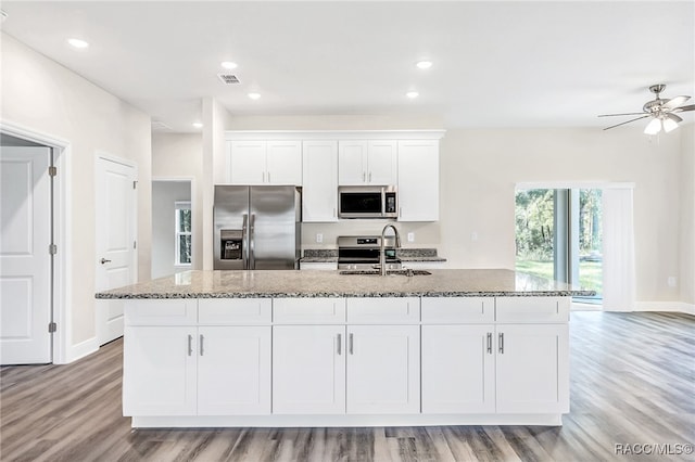 kitchen with appliances with stainless steel finishes, light wood-type flooring, a kitchen island with sink, sink, and white cabinetry