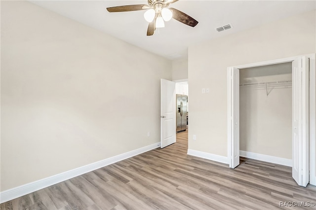 unfurnished bedroom with stainless steel fridge, a closet, ceiling fan, and light wood-type flooring