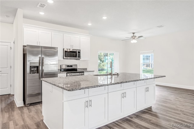 kitchen with a kitchen island with sink, stone counters, sink, appliances with stainless steel finishes, and white cabinetry