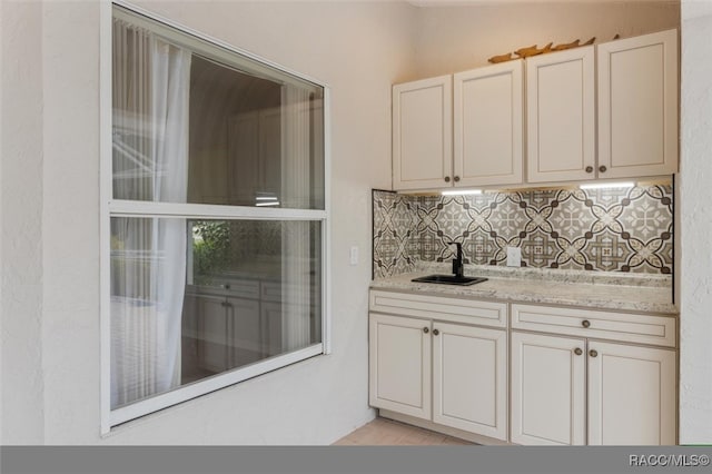 bar with white cabinets, sink, tasteful backsplash, light hardwood / wood-style floors, and light stone counters