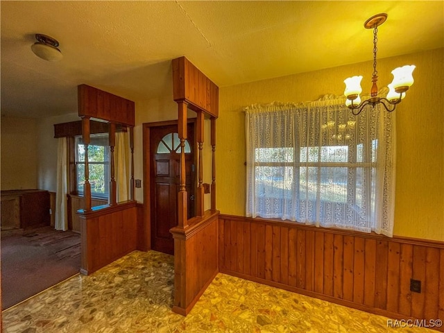 unfurnished dining area featuring wooden walls and a chandelier