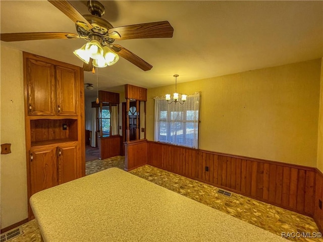 unfurnished dining area with ceiling fan with notable chandelier and wooden walls