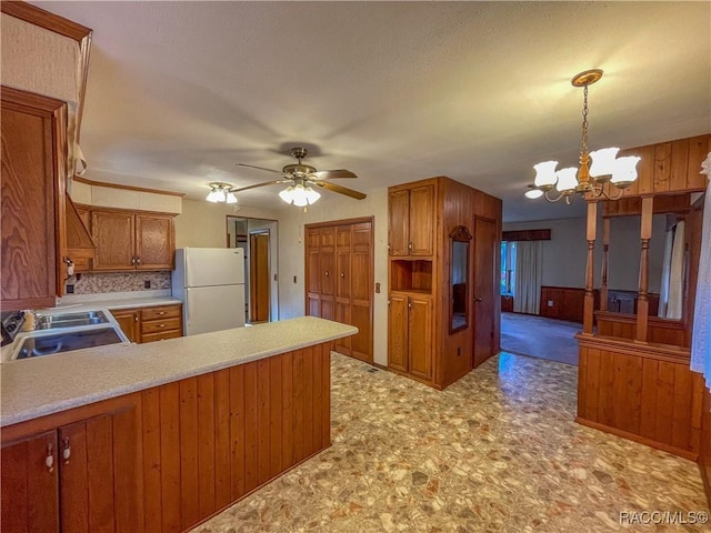 kitchen featuring white refrigerator, kitchen peninsula, ceiling fan with notable chandelier, and hanging light fixtures