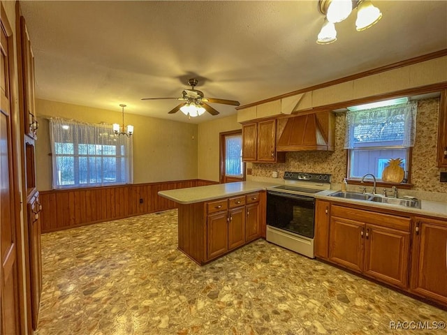 kitchen featuring pendant lighting, sink, wall chimney range hood, electric range oven, and kitchen peninsula