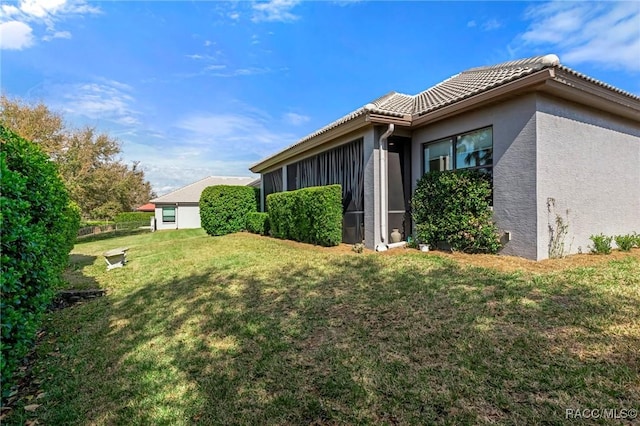 view of side of property with stucco siding, a tile roof, and a yard