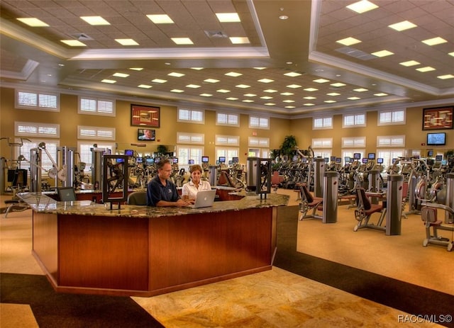 gym featuring a tray ceiling, ornamental molding, and a high ceiling