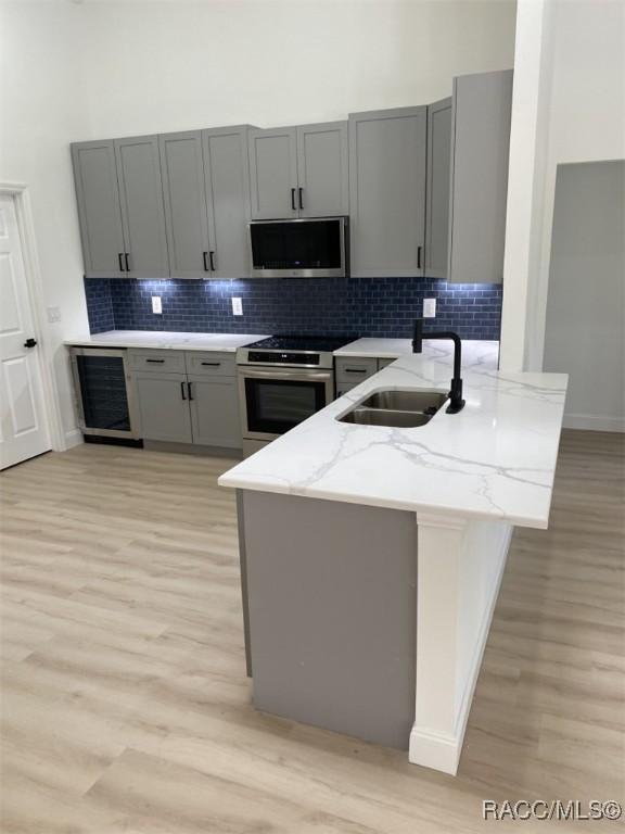 259 N Cherry Pop Dr, Inverness, FL 34453 - kitchen with a sink, appliances with stainless steel finishes, gray cabinetry, light wood-type flooring, and a towering ceiling