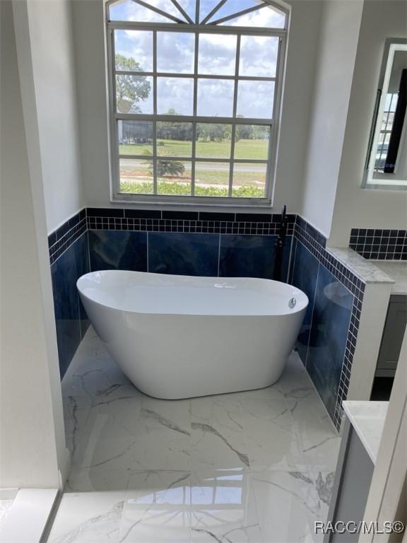 259 N Cherry Pop Dr, Inverness, FL 34453 - bathroom with tile walls, vanity, wainscoting, a freestanding tub, and marble tiled flooring
