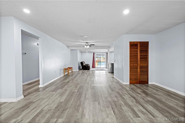 interior space with a textured ceiling, ceiling fan, and light hardwood / wood-style flooring