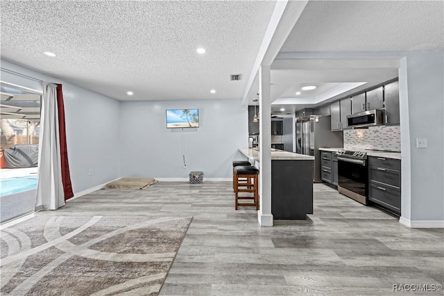 kitchen with a breakfast bar area, appliances with stainless steel finishes, backsplash, a textured ceiling, and light hardwood / wood-style flooring