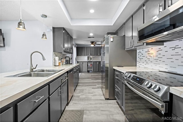 kitchen featuring appliances with stainless steel finishes, decorative backsplash, a tray ceiling, pendant lighting, and sink