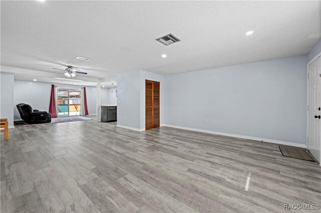 unfurnished living room with a textured ceiling, ceiling fan, and light wood-type flooring