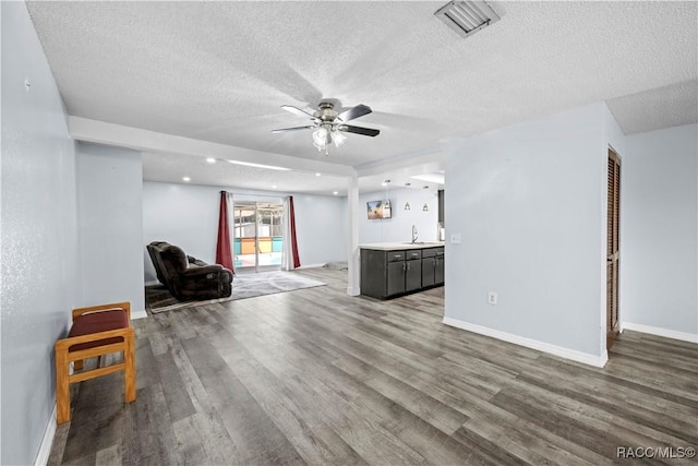 unfurnished living room featuring ceiling fan, wood-type flooring, sink, and a textured ceiling