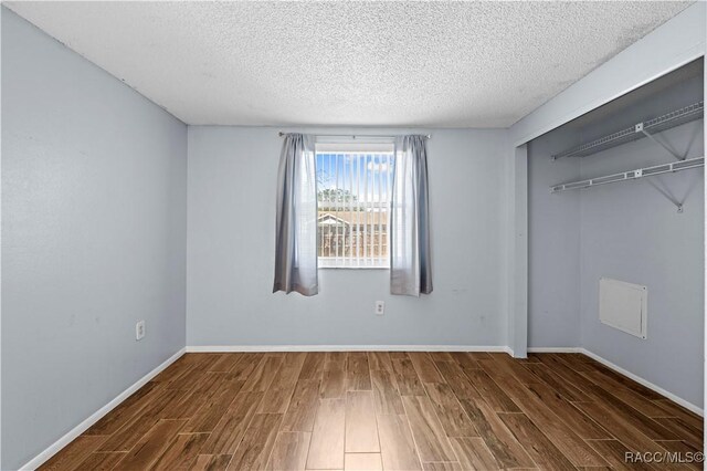 unfurnished bedroom featuring a textured ceiling, dark hardwood / wood-style floors, and a closet