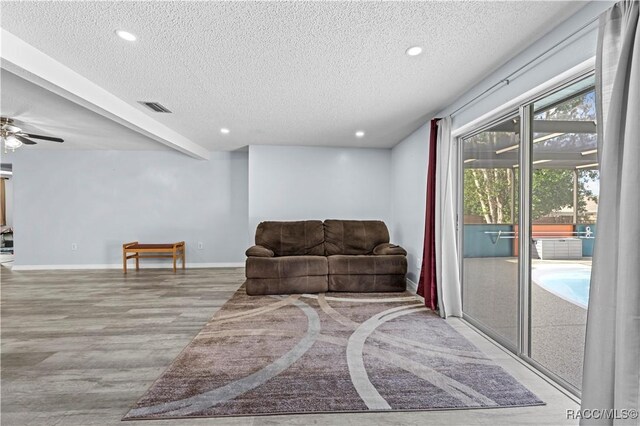 sitting room featuring a textured ceiling, ceiling fan, light hardwood / wood-style floors, and beamed ceiling