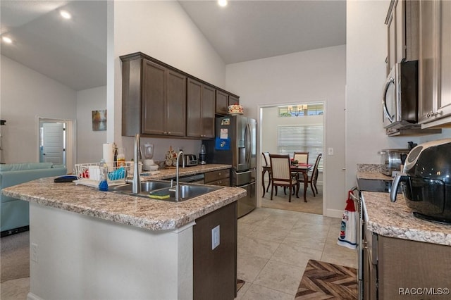 kitchen with light tile patterned floors, stainless steel appliances, dark brown cabinetry, a sink, and high vaulted ceiling