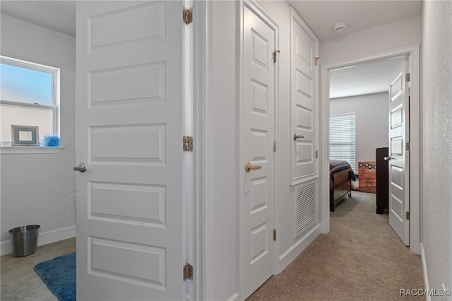 corridor featuring a healthy amount of sunlight, light carpet, and baseboards