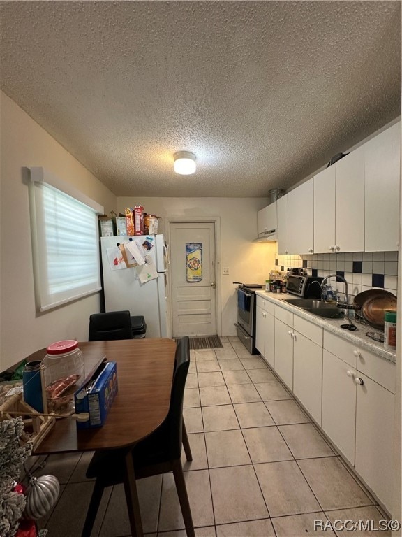 kitchen featuring tasteful backsplash, stainless steel range with electric stovetop, sink, white refrigerator, and white cabinetry