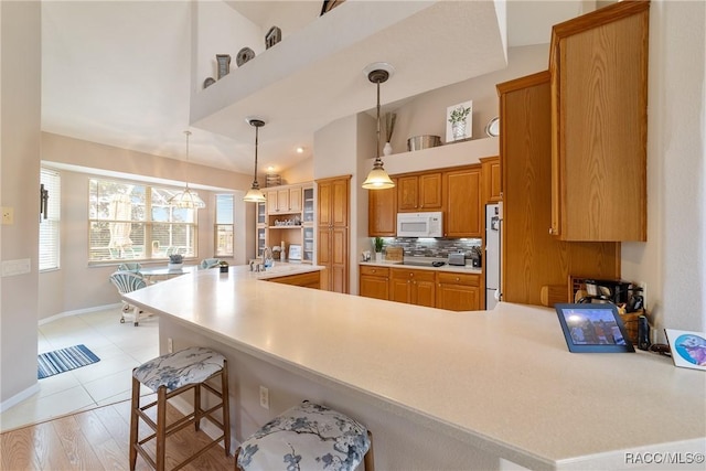 kitchen featuring white appliances, lofted ceiling, a kitchen breakfast bar, tasteful backsplash, and kitchen peninsula