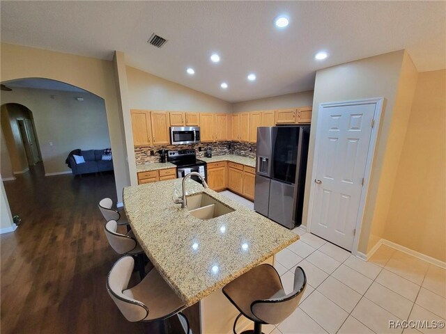 kitchen with appliances with stainless steel finishes, a sink, arched walkways, baseboards, and vaulted ceiling