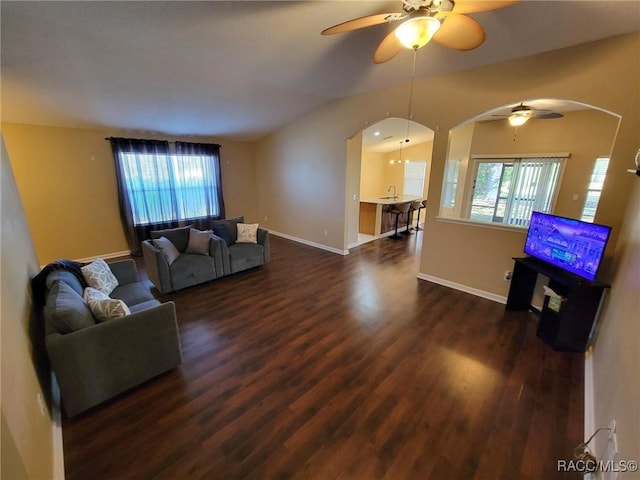 living area featuring arched walkways, ceiling fan, dark wood-style flooring, and baseboards