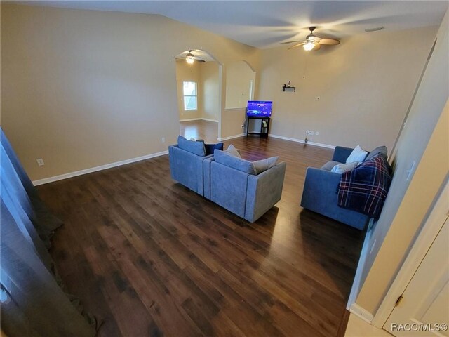 living area featuring a ceiling fan, dark wood-type flooring, baseboards, and arched walkways