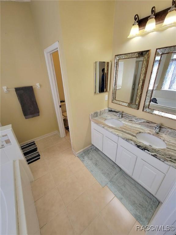 full bath with double vanity, baseboards, tile patterned floors, and a bathtub