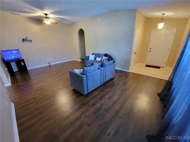 living room with arched walkways, a ceiling fan, dark wood-style floors, baseboards, and vaulted ceiling