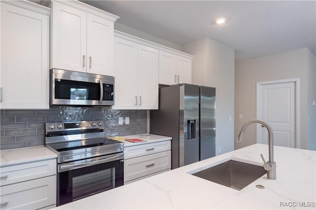 kitchen with stainless steel appliances, sink, white cabinets, and light stone counters