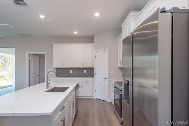 kitchen featuring sink, white cabinets, decorative backsplash, a kitchen island with sink, and stainless steel appliances