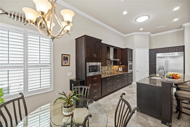 kitchen featuring an inviting chandelier, sink, built in appliances, decorative light fixtures, and light stone counters