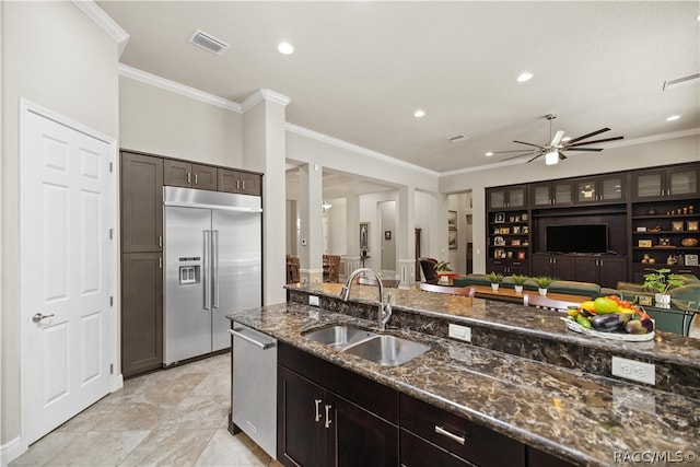 kitchen featuring sink, stainless steel appliances, dark stone counters, dark brown cabinets, and ornamental molding