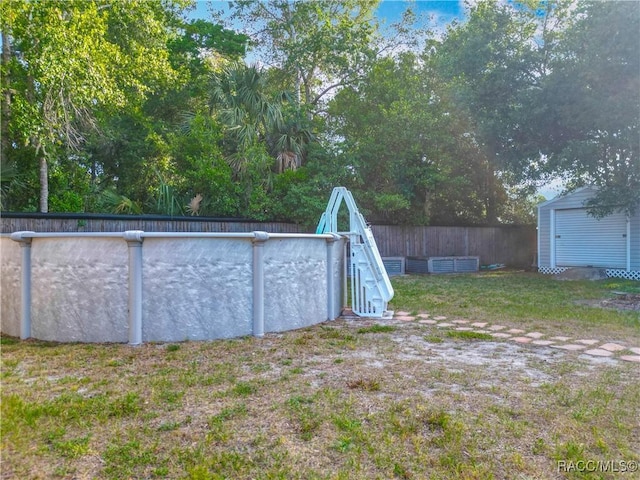 view of yard with a storage shed, an outdoor pool, fence, and an outbuilding