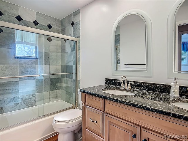 full bath featuring double vanity, a sink, combined bath / shower with glass door, and toilet