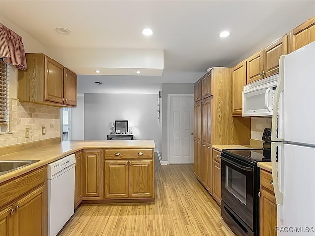 kitchen with a peninsula, light countertops, light wood finished floors, and white appliances