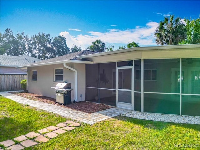 back of property featuring a sunroom, stucco siding, a yard, and fence