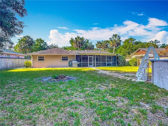 back of property with a sunroom, a lawn, fence, and stucco siding