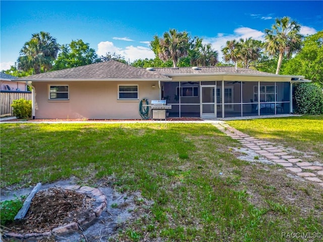 rear view of house featuring fence, ceiling fan, a sunroom, stucco siding, and a lawn