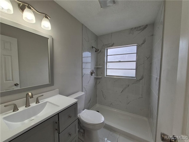 bathroom with toilet, a textured ceiling, tiled shower, and vanity