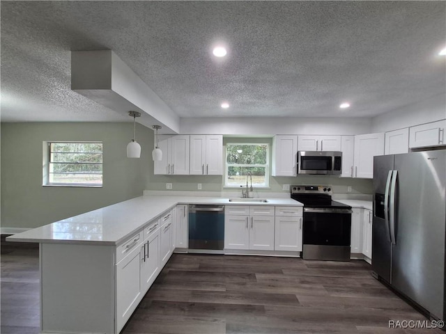 kitchen featuring kitchen peninsula, stainless steel appliances, hanging light fixtures, white cabinets, and sink