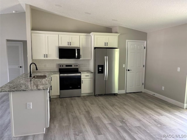 kitchen featuring appliances with stainless steel finishes, a sink, vaulted ceiling, light wood-style floors, and backsplash