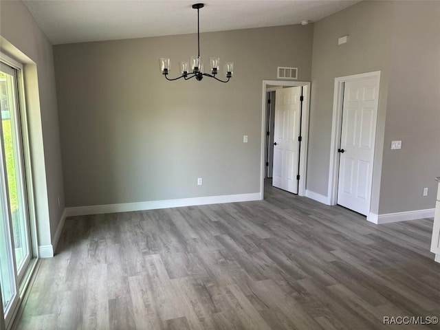 unfurnished dining area featuring a chandelier, wood finished floors, baseboards, and high vaulted ceiling