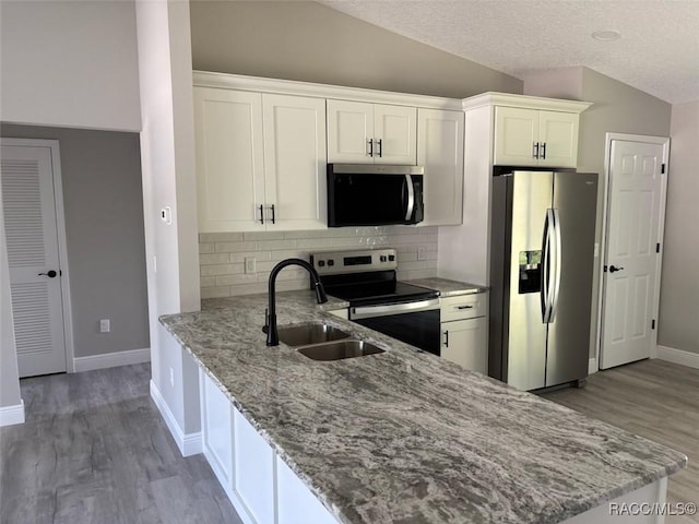 kitchen featuring stainless steel appliances, a sink, vaulted ceiling, light wood-type flooring, and backsplash